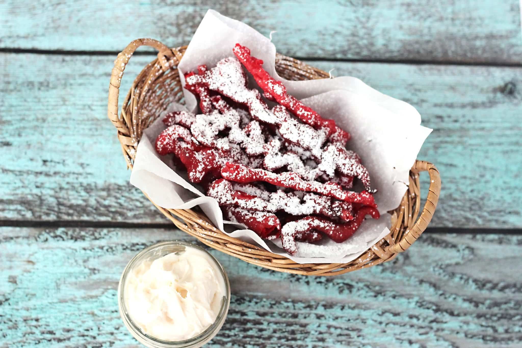 Whether you call them funnel cake fries or funnel cake sticks, this copycat recipe of the beloved fair food is served red velvet style with cream cheese frosting for dipping. It's a dessert to die for!