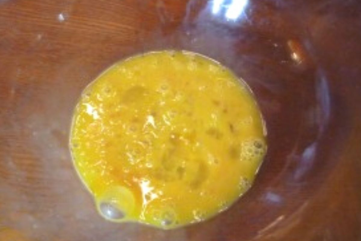 two raw eggs cracked into a glass bowl and whisked together.