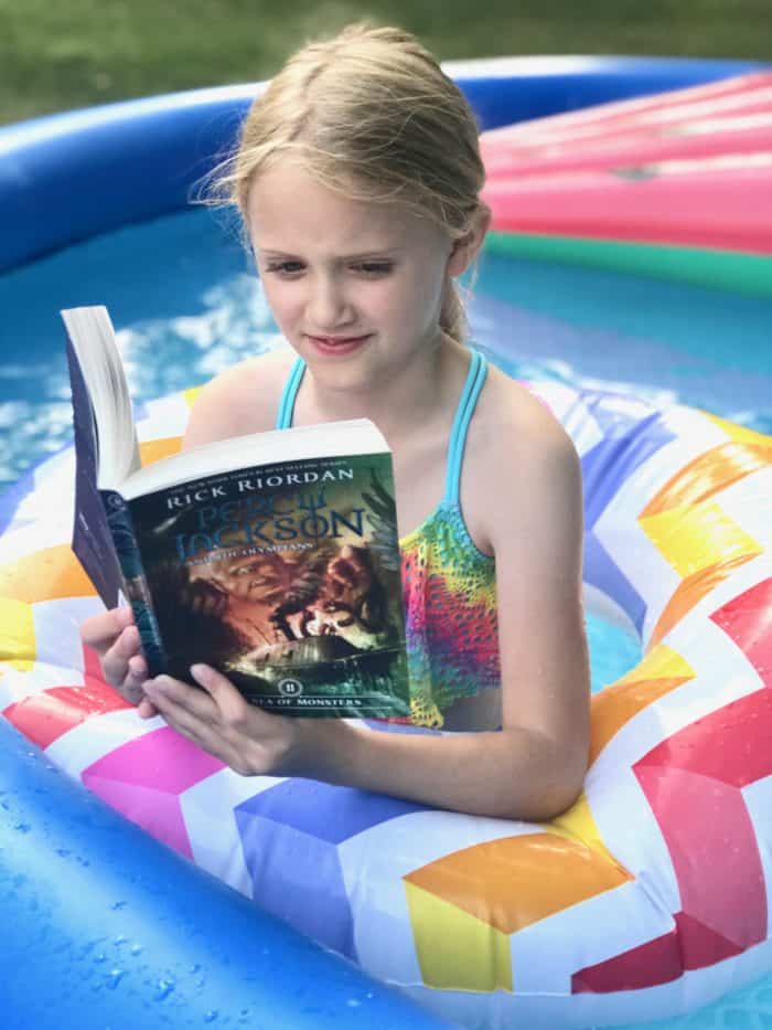 girl floating in a pool reading a percy jackson book