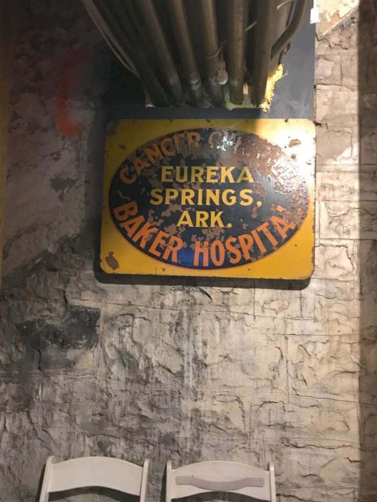 A rusted metal sign in the basement of the crescent hotel that reads "cancer center baker hospital eureka springs Arkansas."