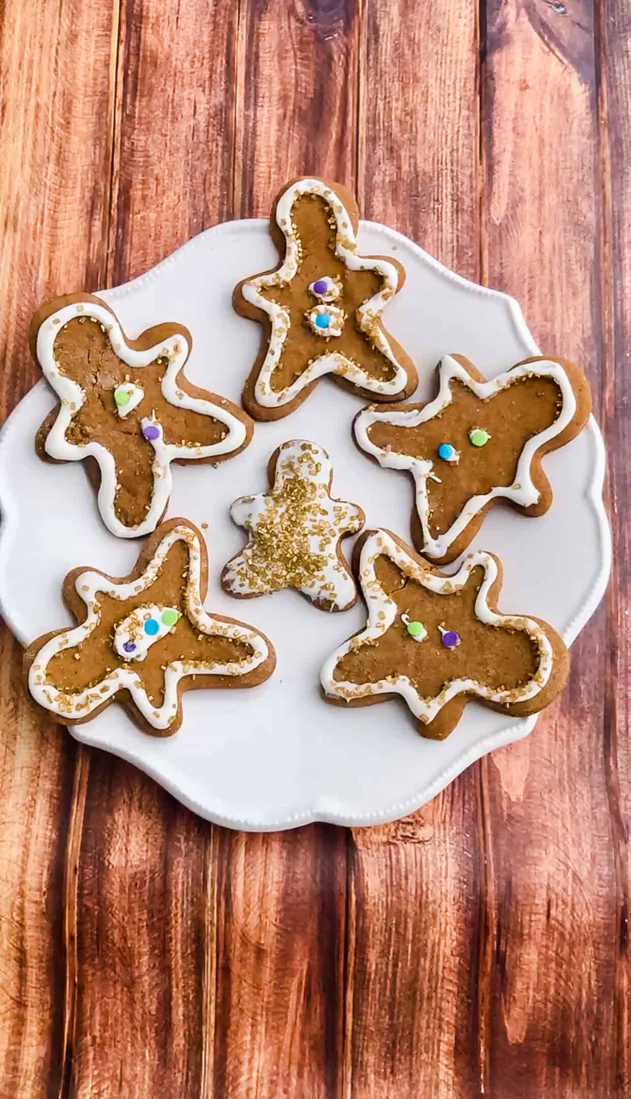 A plate of six classic gingerbread man cookies in two different sizes decorated with white icing and gold sprinkles.