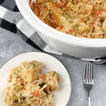 crock pot chicken and dumplings finished recipe in a white crock pot with a single serving displayed on a plate.