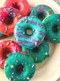 a plate of multicolored rainbow unicorn donuts with stripes and sprinkles