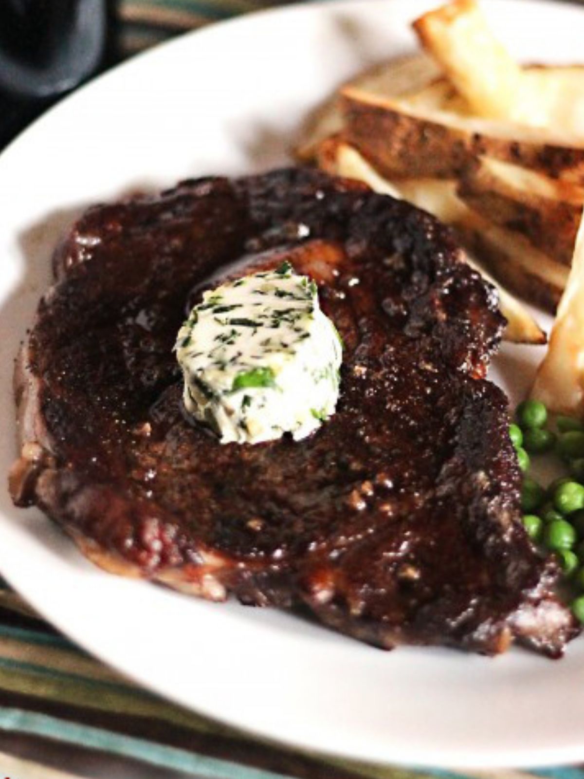 prepared chuck eye steak resting on a white plate and topped with herbed butter