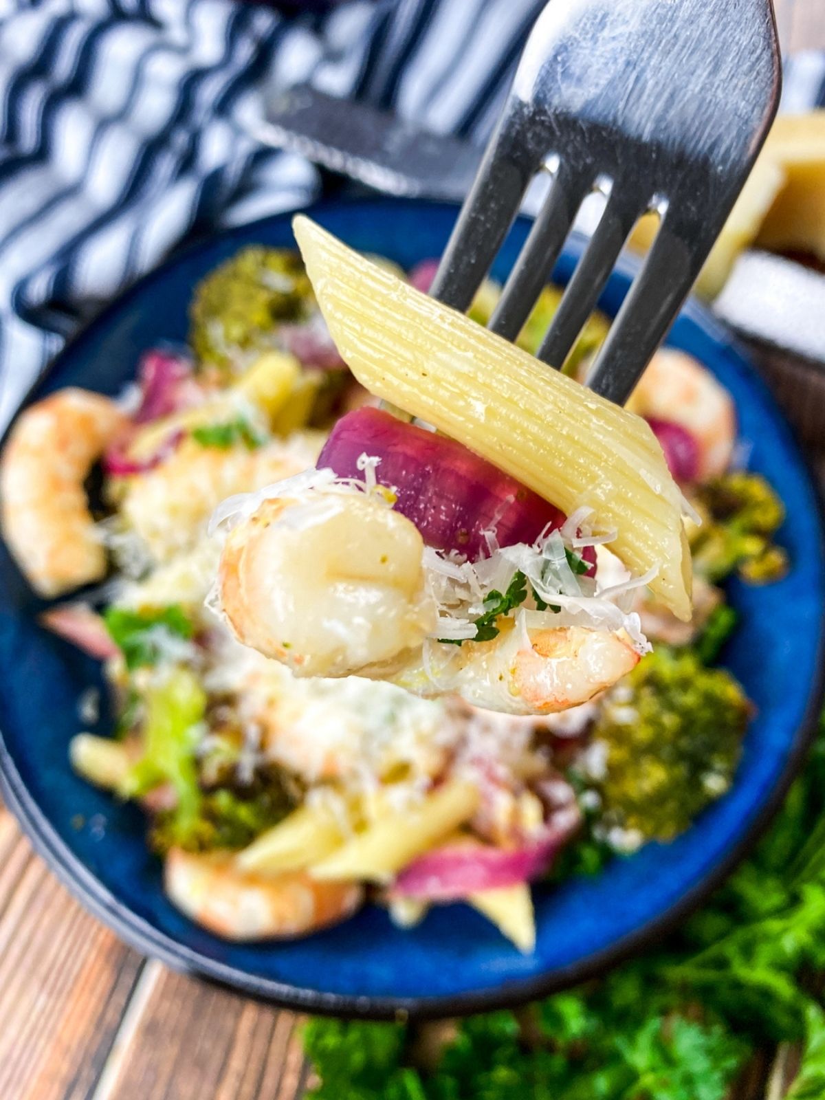 a plate of garlic shrimp pasta with a single bite of shrimp, penne, and red onion on a fork in the foreground.