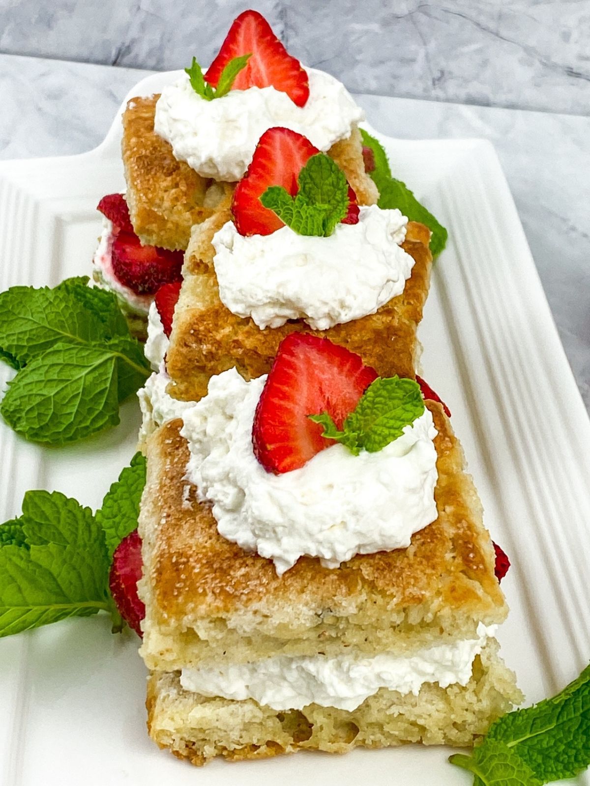 Three prepared strawberry shortcakes assembled and garnished with mint sprigs.