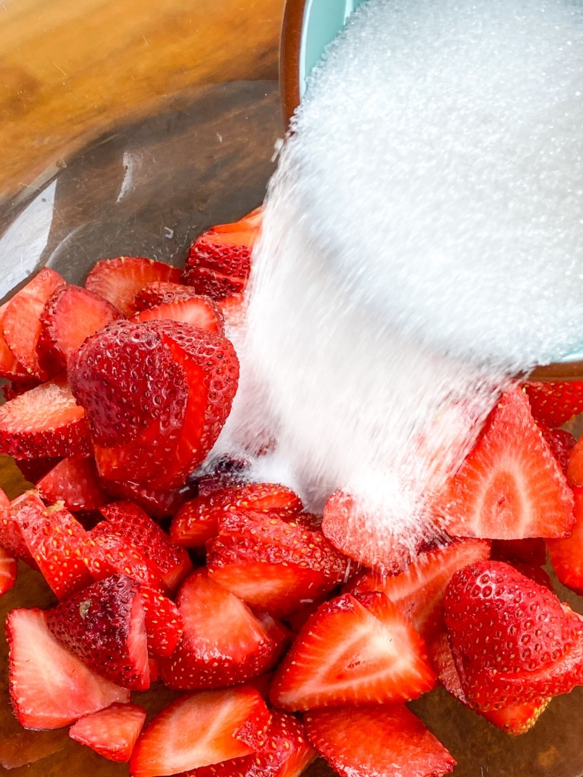 White, granulated sugar being poured on top of fresh strawberries.