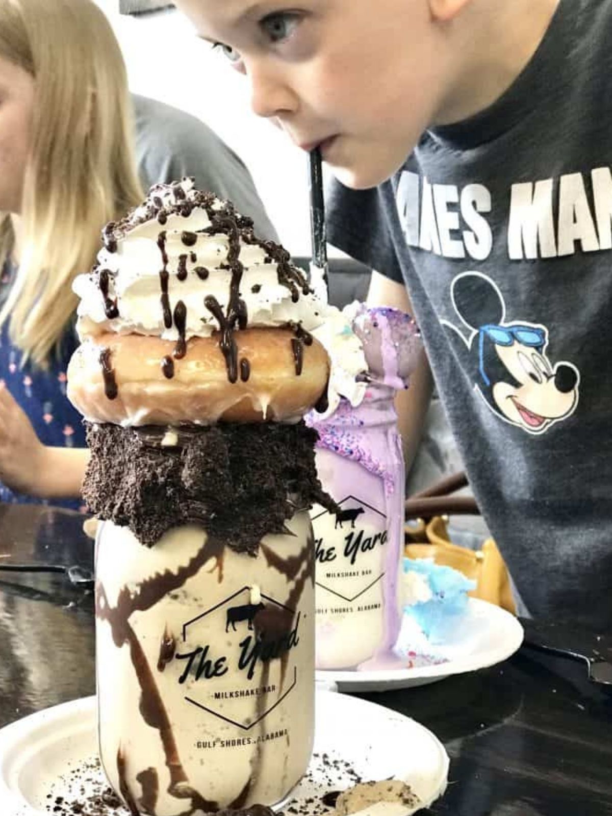 white milkshake in a mason jar topped with oreo cookies, a donut, whipped cream, and chocolate syrup