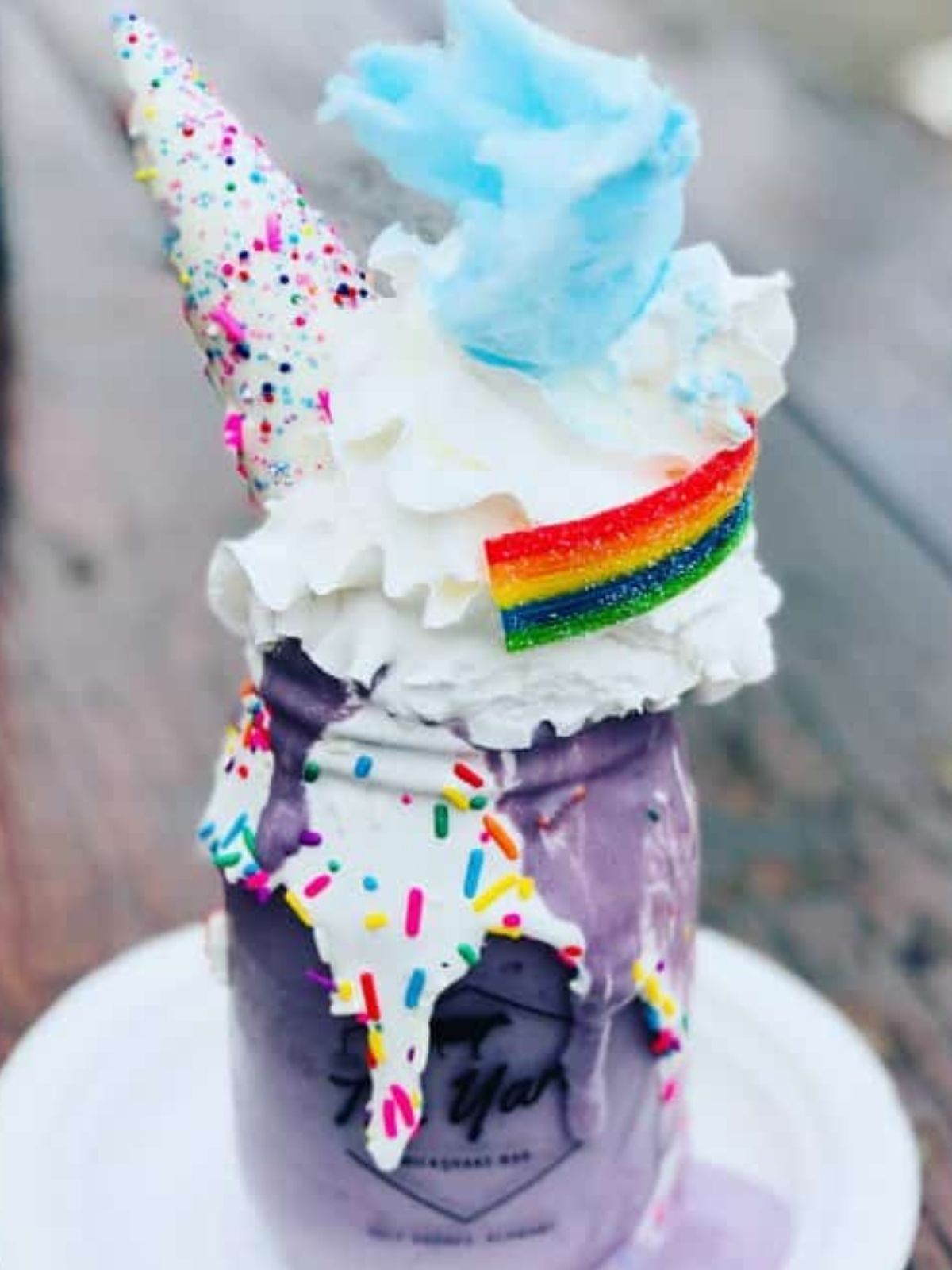 a unicorn milkshake that's purple and served in a mason jar. It's topped with whipped cream, an ice cream come, cotton candy, and a rainbow gummy