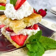 classic strawberry shortcake assembled with strawberries and whipped cream on a plate with a mint garnish.