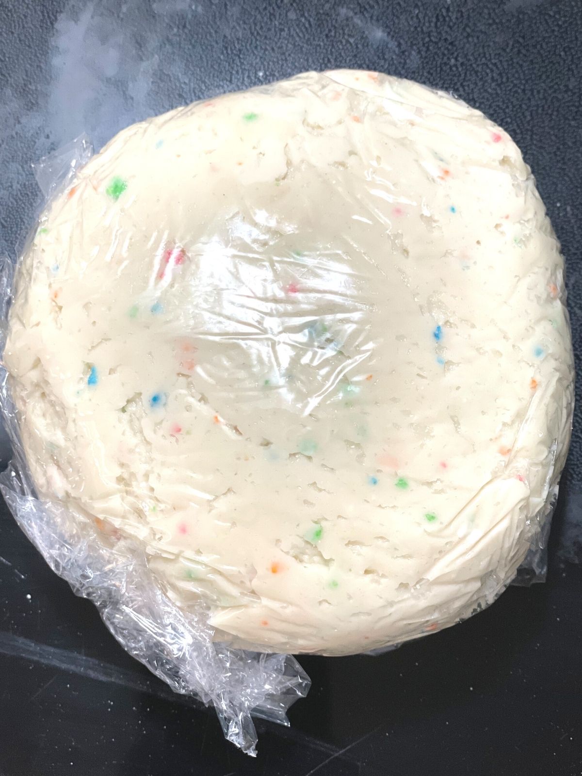 funfetti dip formed into a ball and covered in plastic wrap ready to go into the refrigerator or freezer.