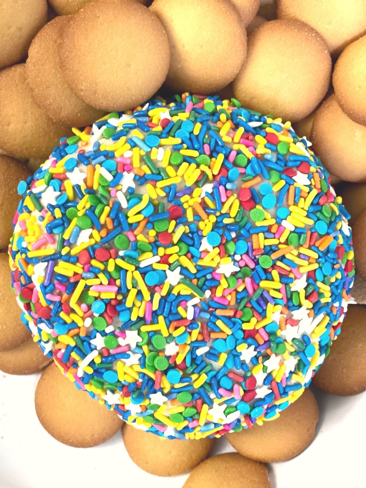 a sprinkle covered cream cheese ball surrounded by vanilla wafers and graham crackers for dipping. 