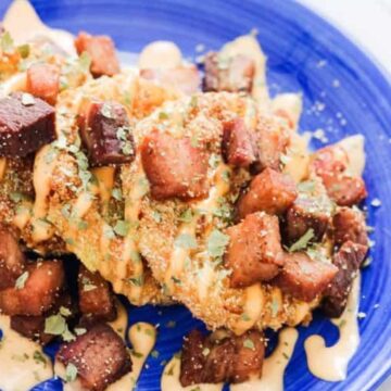 fried green tomatoes arranged on a blue plate and drizzled with dipping sauce.
