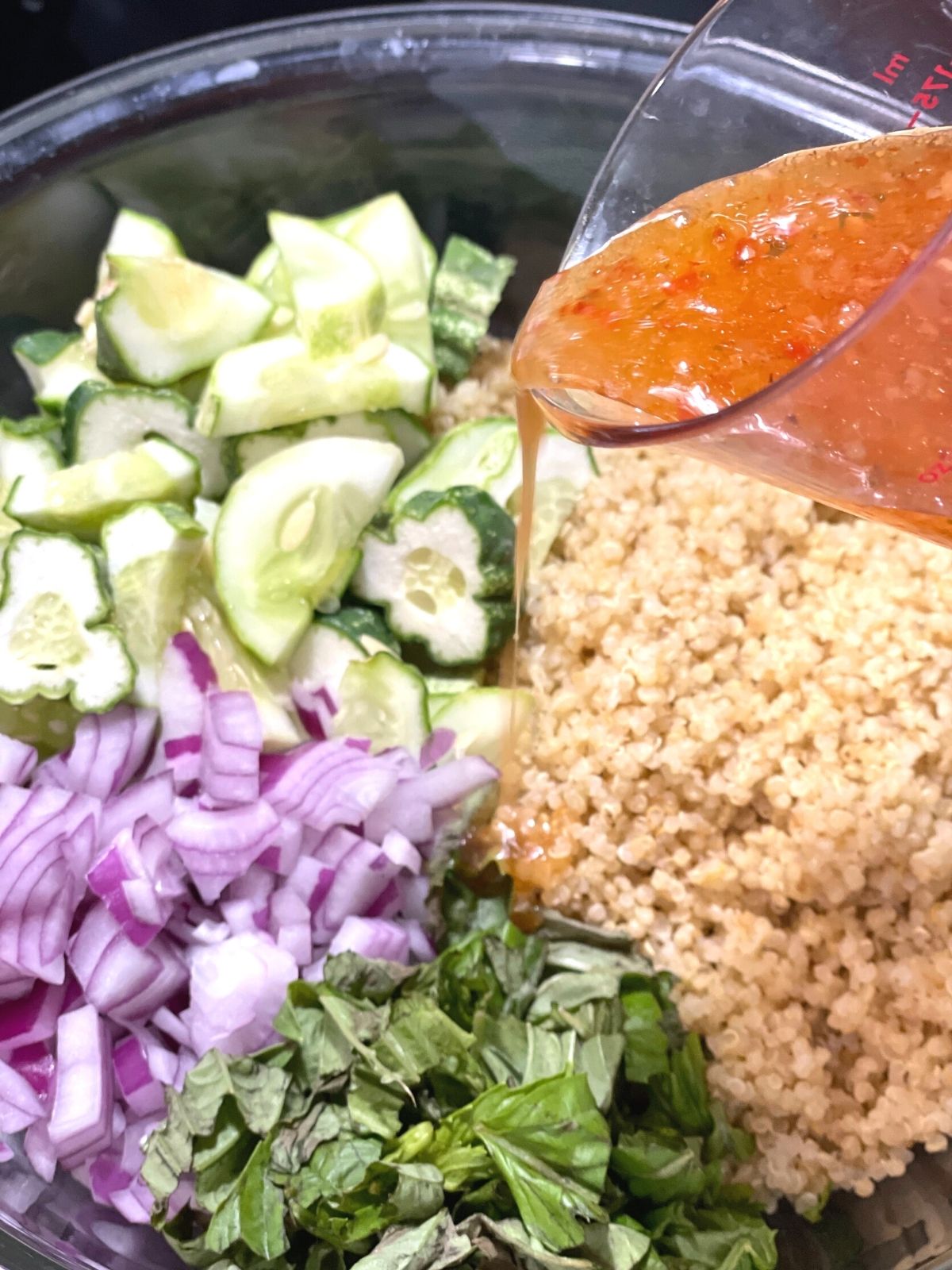 pouring italian dressing into a bowl of cucumber salad ingredients.