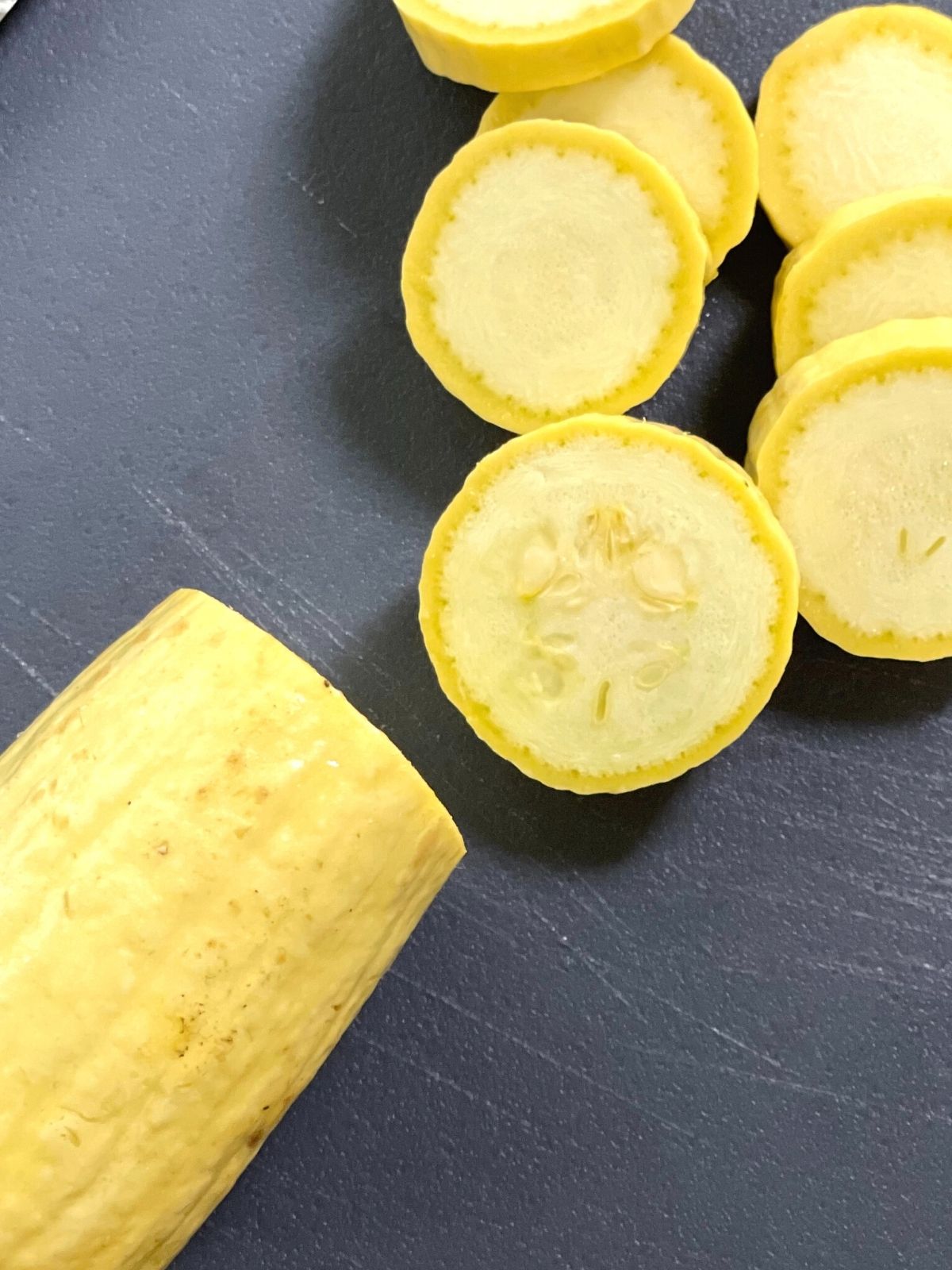 A whole yellow squash being sliced into ¼ inch round slices.