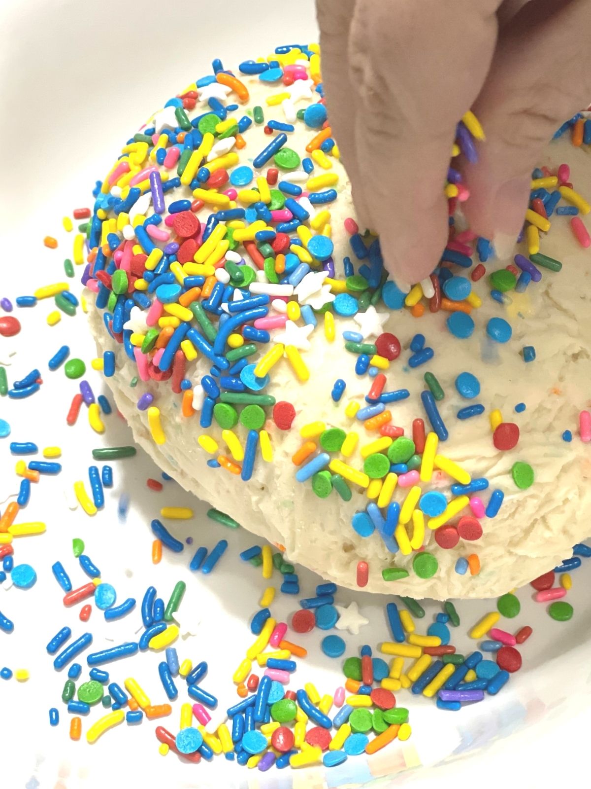 Pressing sprinkles into the finished dessert cheese ball made with funfetti cake mix.