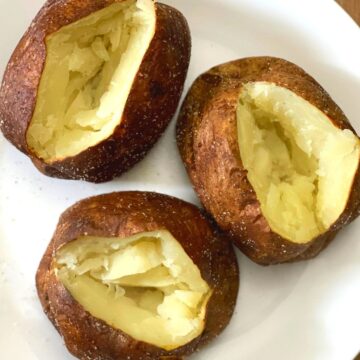 Three fully baked russet potatoes sliced, squeezed and displayed on a white plate. They are ready to eat.