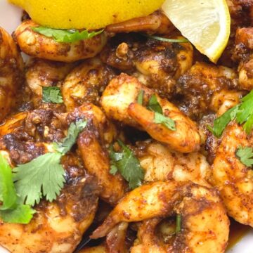 A close up of a bowl of blackened shrimp topped with cilantro. Lemon wedges are used as a garnish.