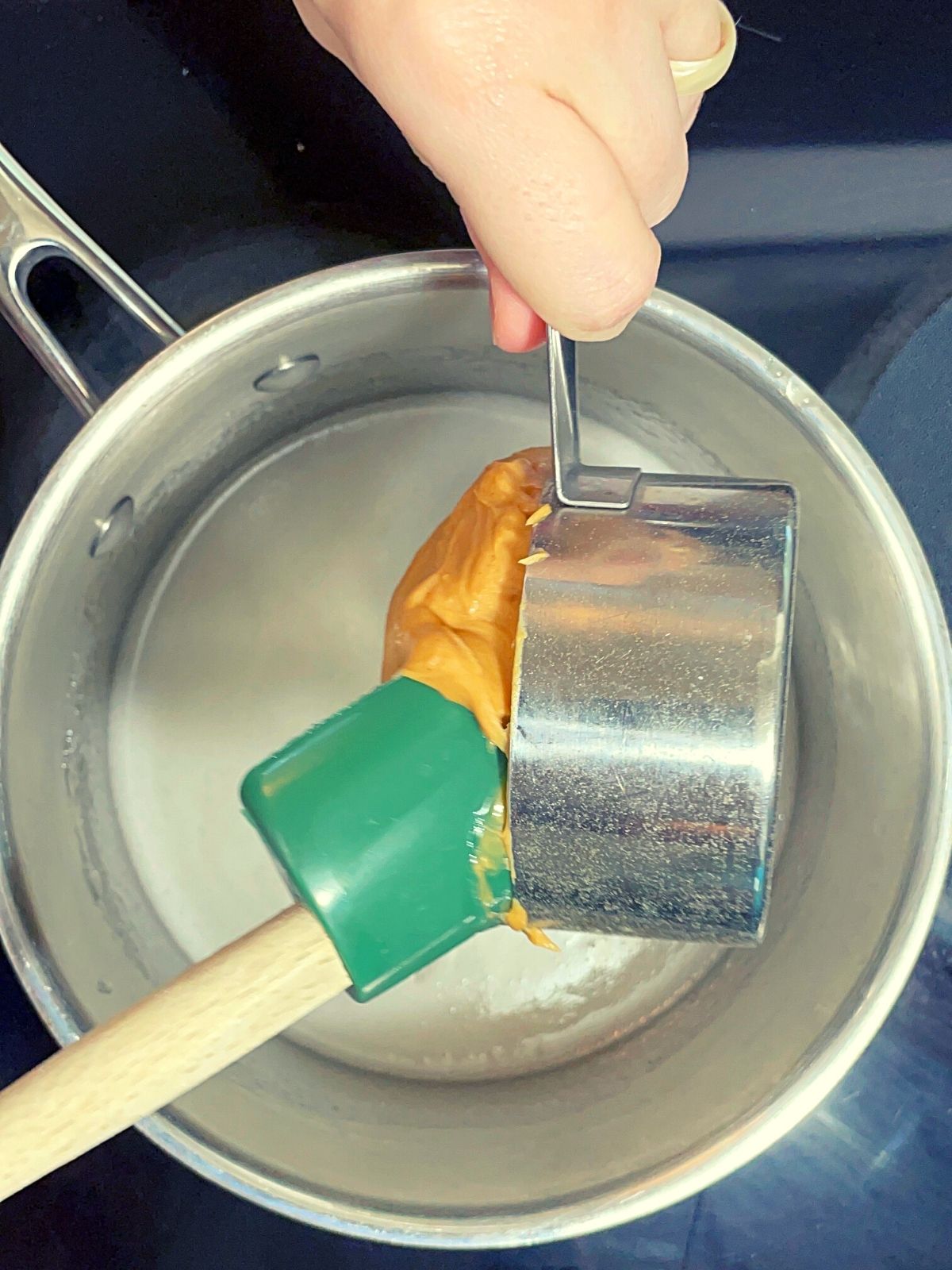Adding peanut butter to a saucepan filled with hot corn syrup and sugar mixture.