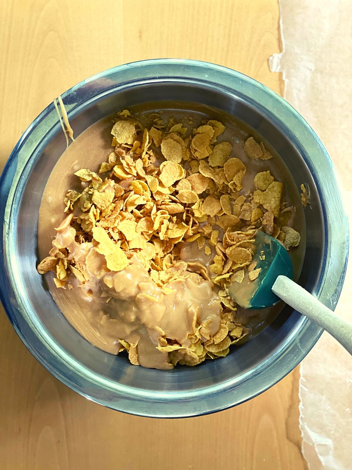 mixing bowl full of cornflakes with the peanut butter mixture poured over the top.