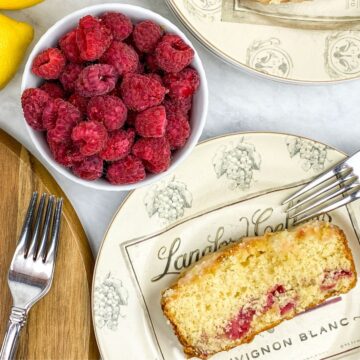 a slice of lemon loaf cake with raspberries in a bowl in the background.