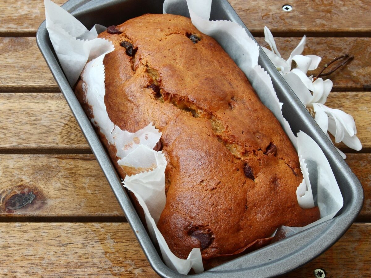 A baked quick bread still in the loaf pan lined with parchment paper for easy cleanup.