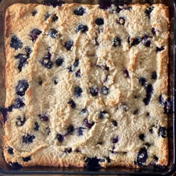 Fully baked blueberry coffee cake in a square glass baking pan ready to slice into squares.