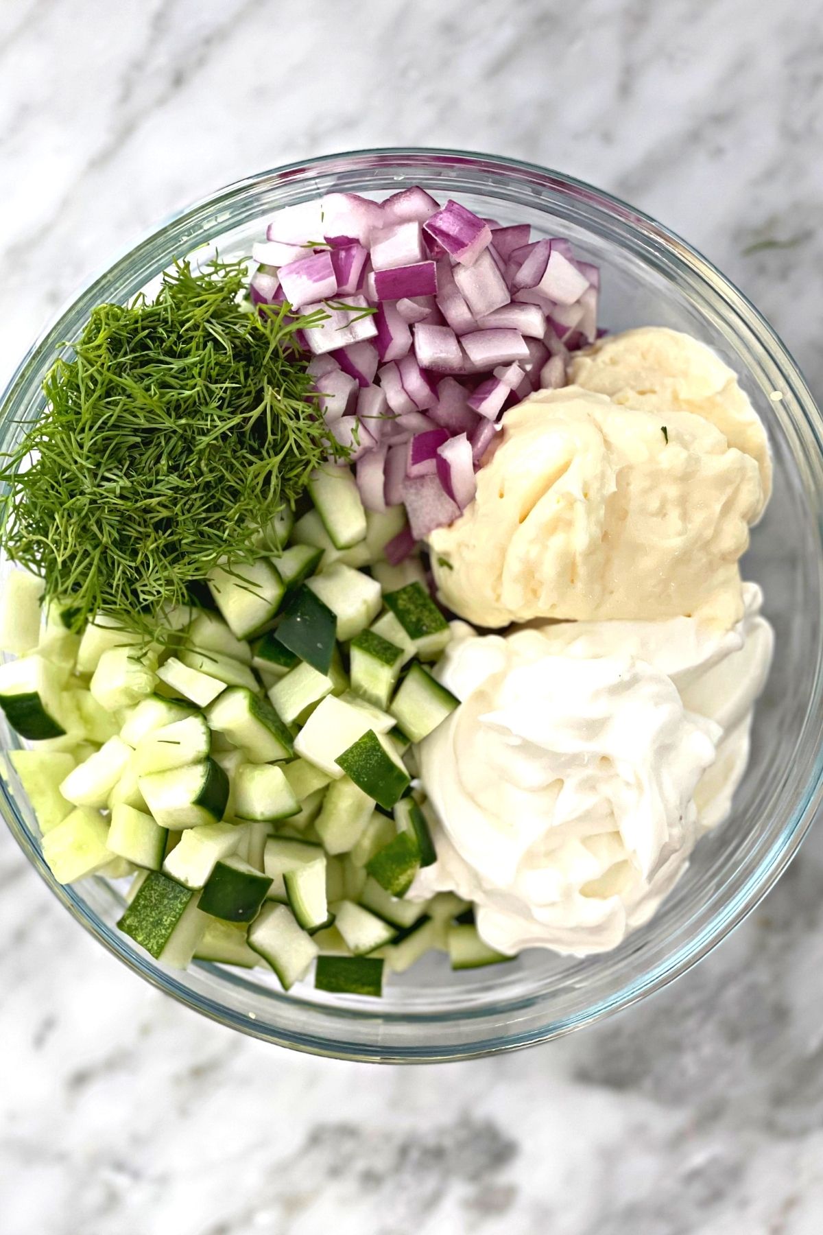 Creamy cucumber salad ingredients prepared and placed in a glass bowl ready to be mixed.