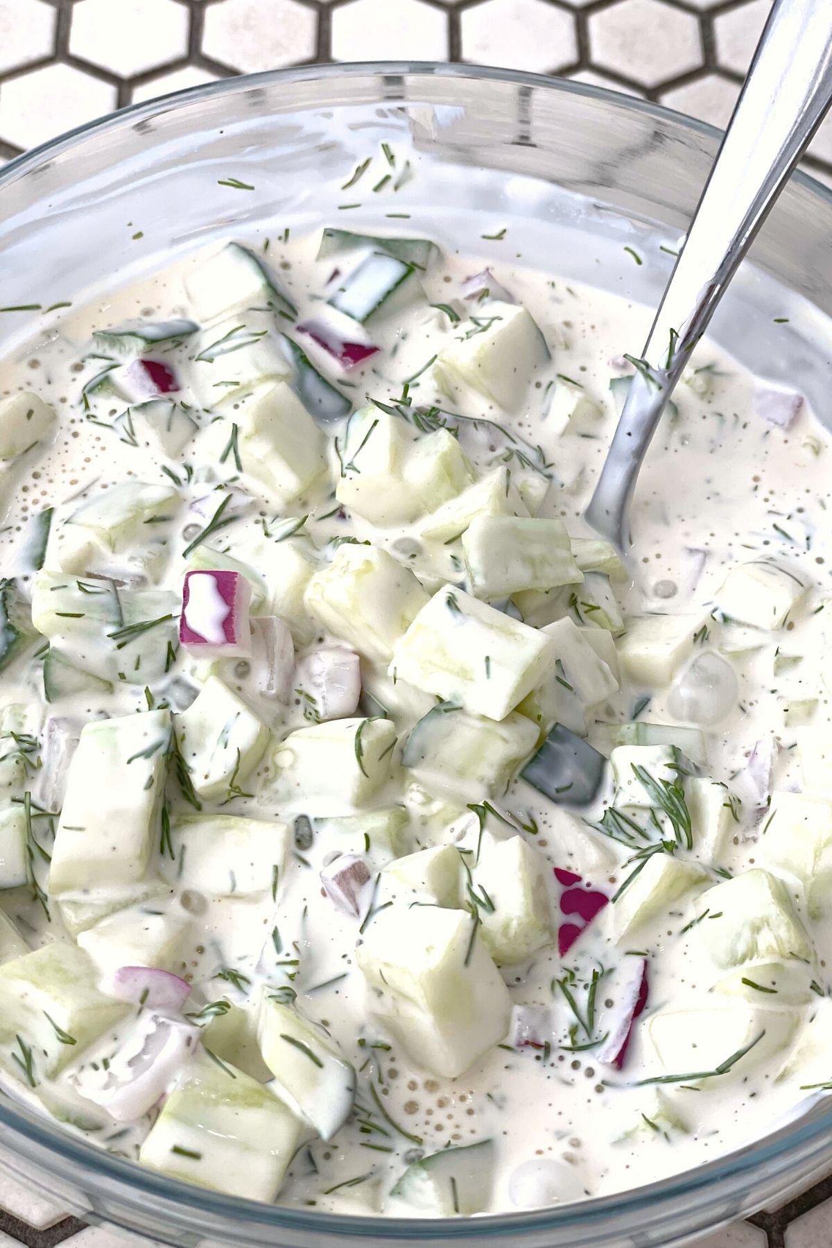 a bowl of creamy cucumber salad mixed together and ready to chill in the refrigerator.