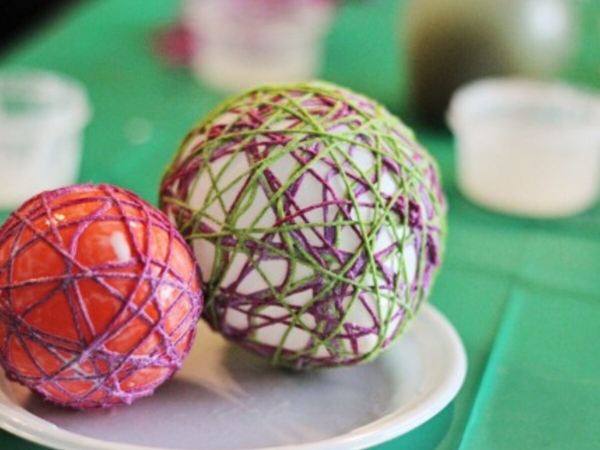 Two balloons with glue-soaked embroidery floss wrapped around them drying on a Styrofoam plate.