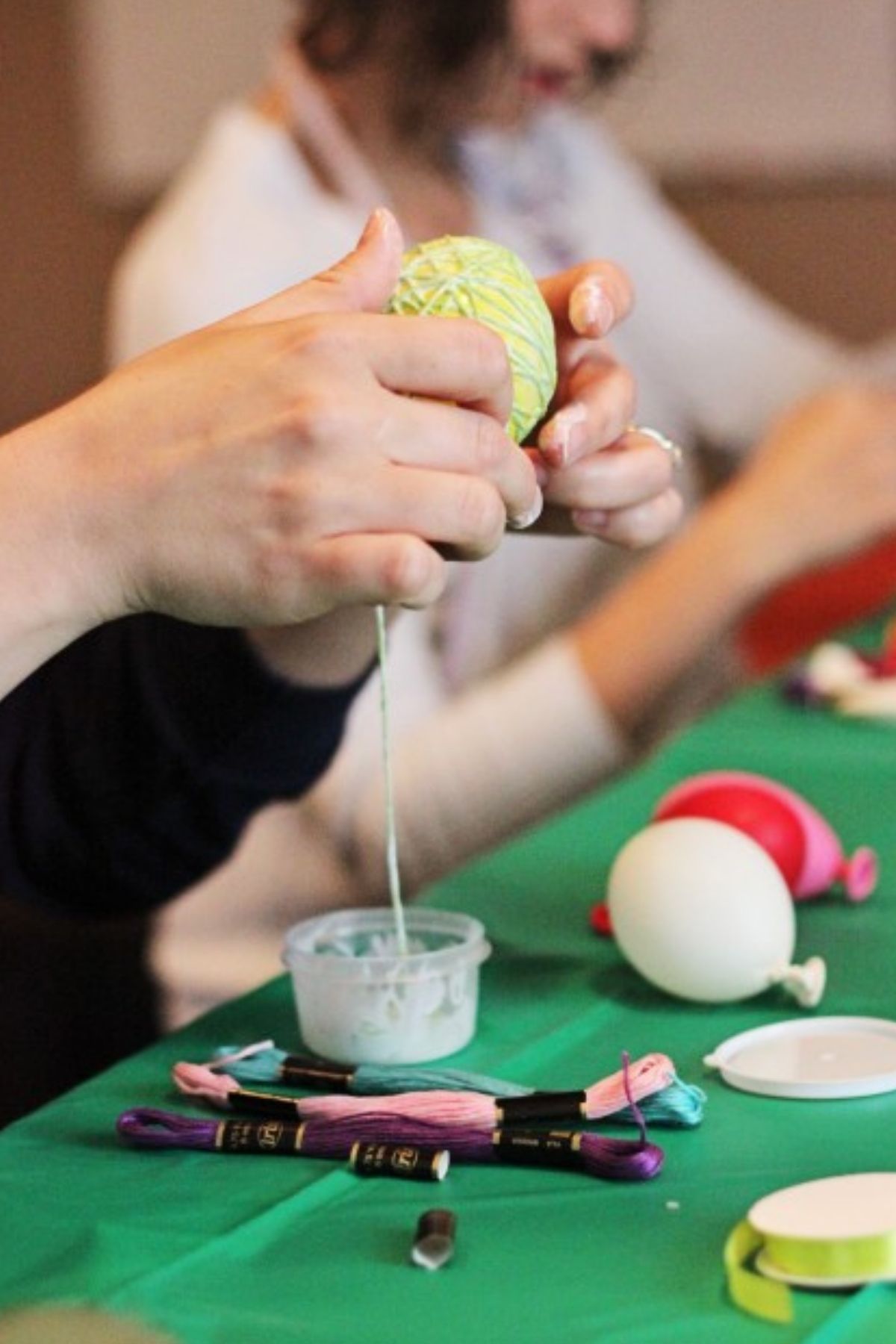 Winding lime green embroidery floss soaked in glue mixture around a small balloon.