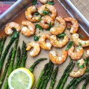 Baked shrimp and asparagus on a sheet pan with lemon slices arranged on top.