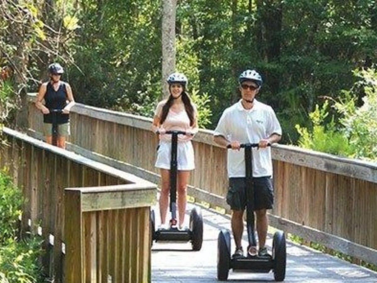 Three people riding segways over a wooden raised path in Gulf State Park.