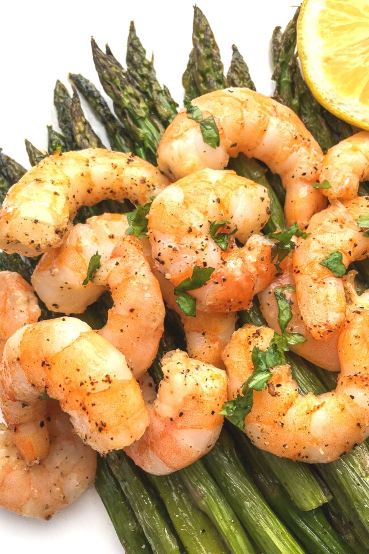 Close up shot of baked shrimp resting on a bed of asparagus.