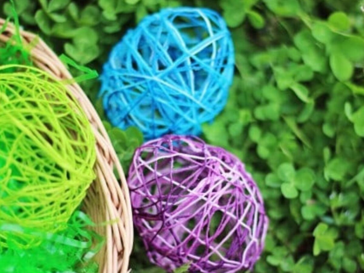 Three easter eggs made of string and mod podge resting in a nest of clover.