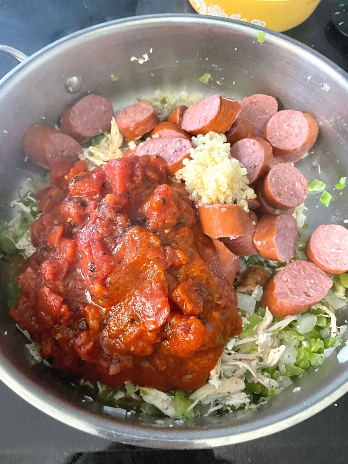 Sliced andouille sausage, crushed tomatoes and garlic added to a pan of cooked chicken and vegetables.