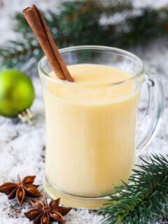 A serving of non alcoholic homemade eggnog in a clear glass mug with a cinnamon stick for garnish.