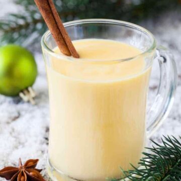 A serving of non alcoholic homemade eggnog in a clear glass mug with a cinnamon stick for garnish.