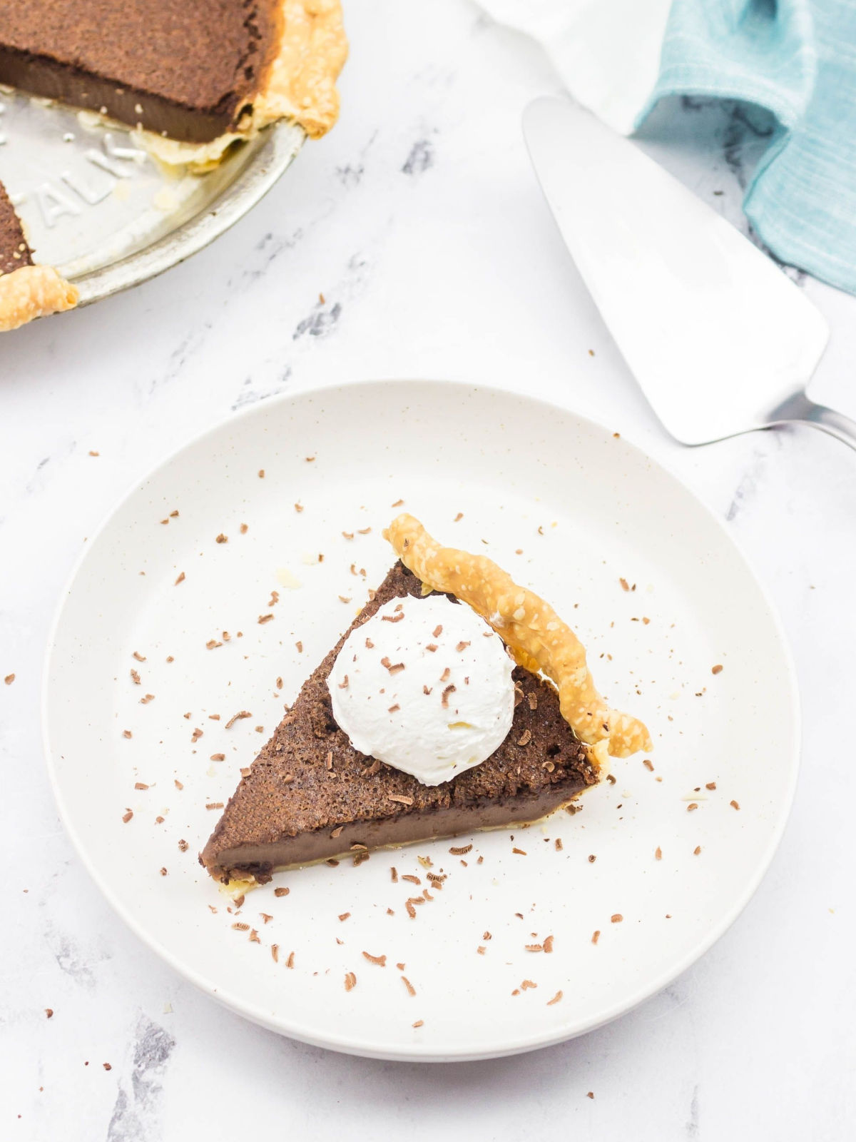 Slice of chocolate chess pie topped with whipped cream on a plate.