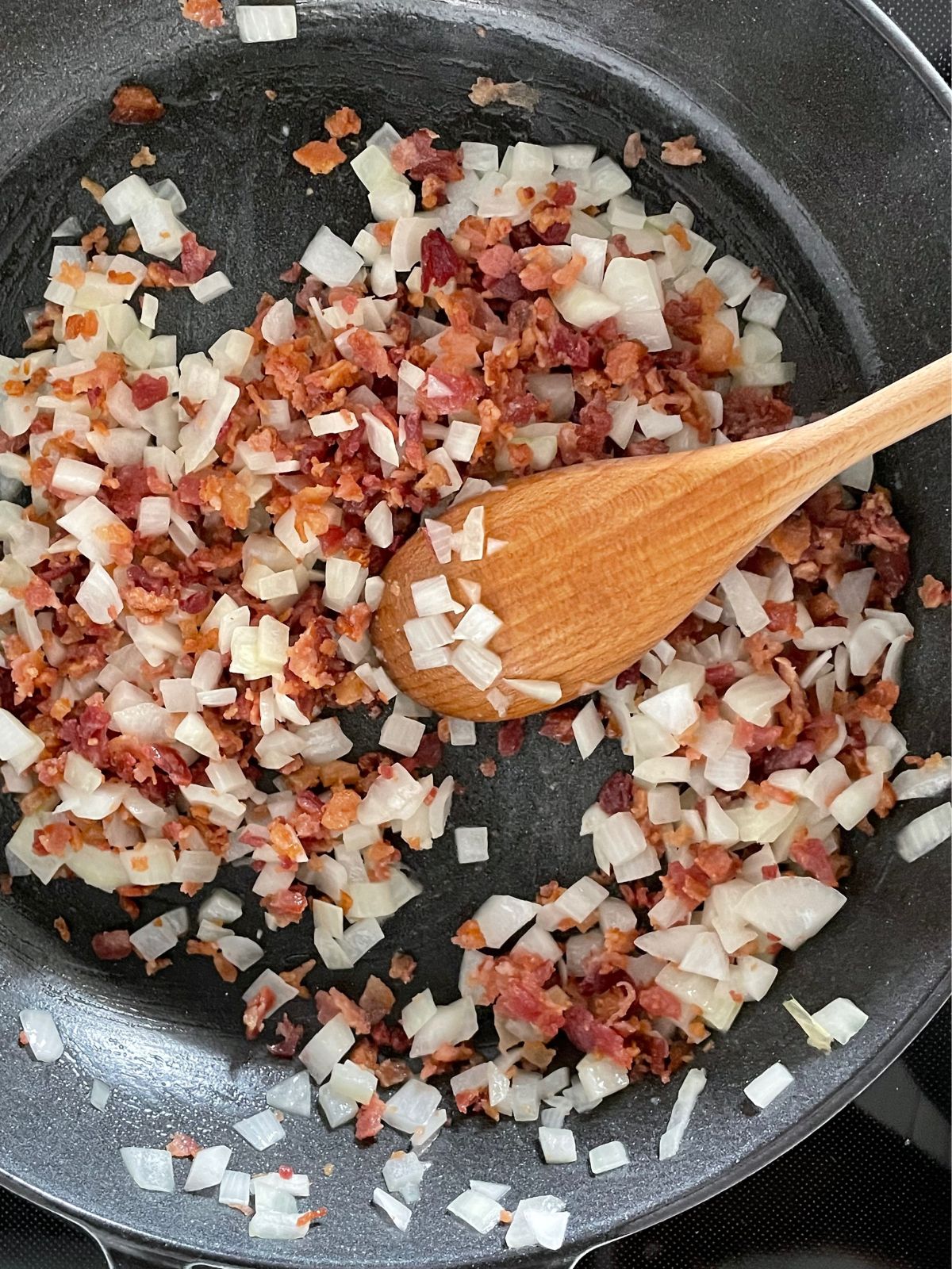 Adding bacon to a hot skillet full of diced onions and butter.