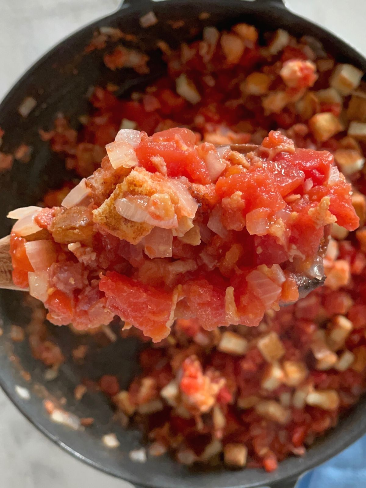 An iron skillet full of authentic Southern stewed tomatoes with a wooden spoon lifting a bite out of the pan.