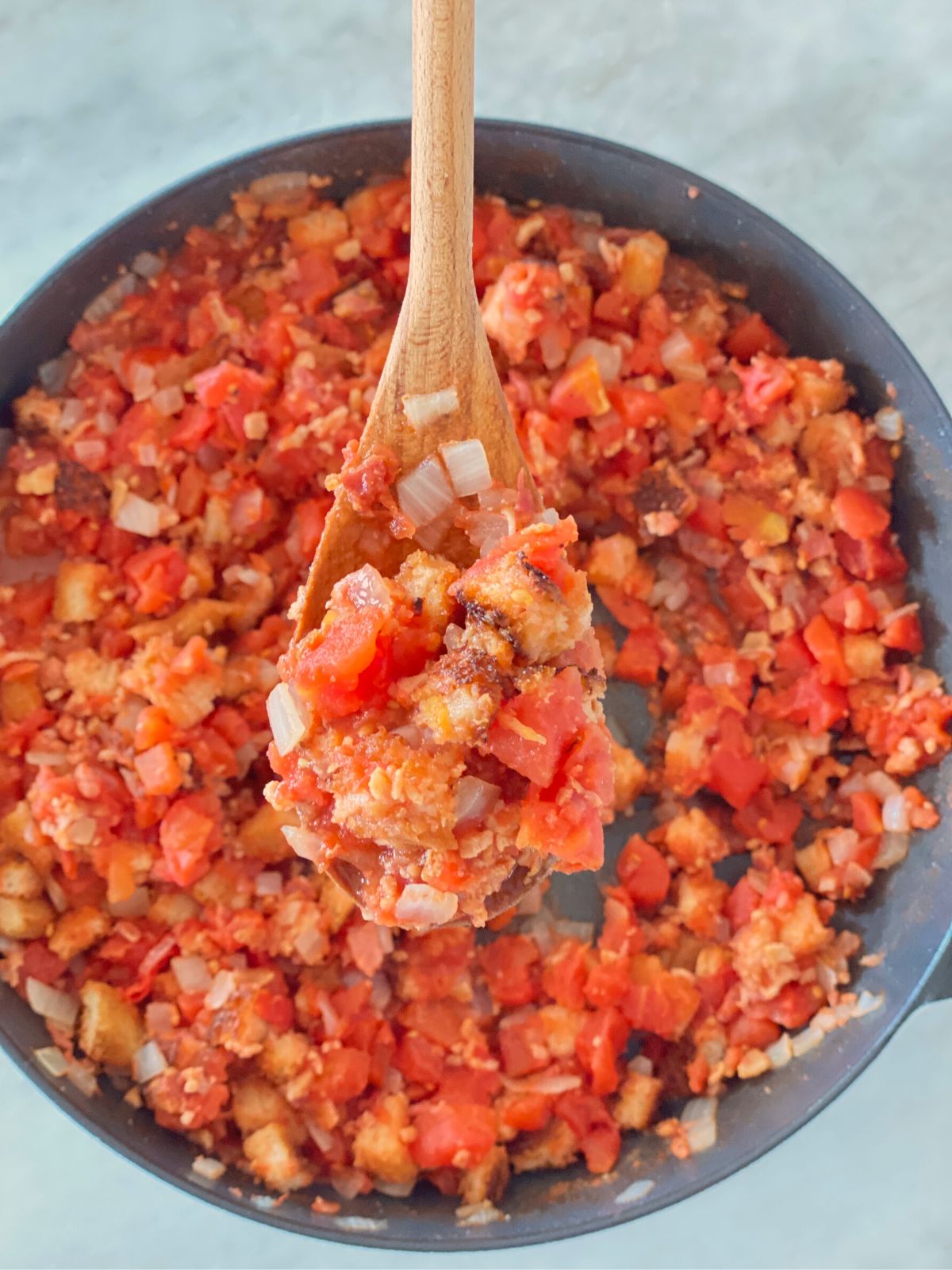 An iron skillet full of authentic Southern stewed tomatoes with a wooden spoon lifting a bite out of the pan.