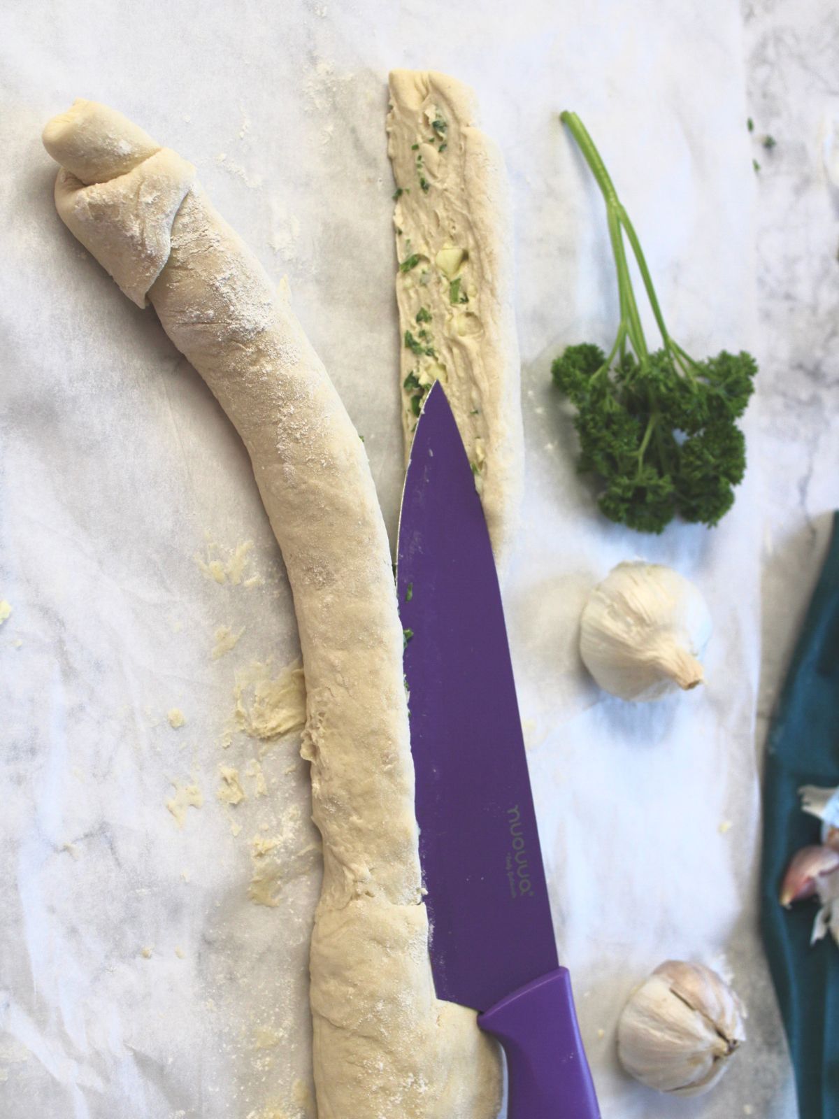 Garlic bread dough log being sliced in half vertically.