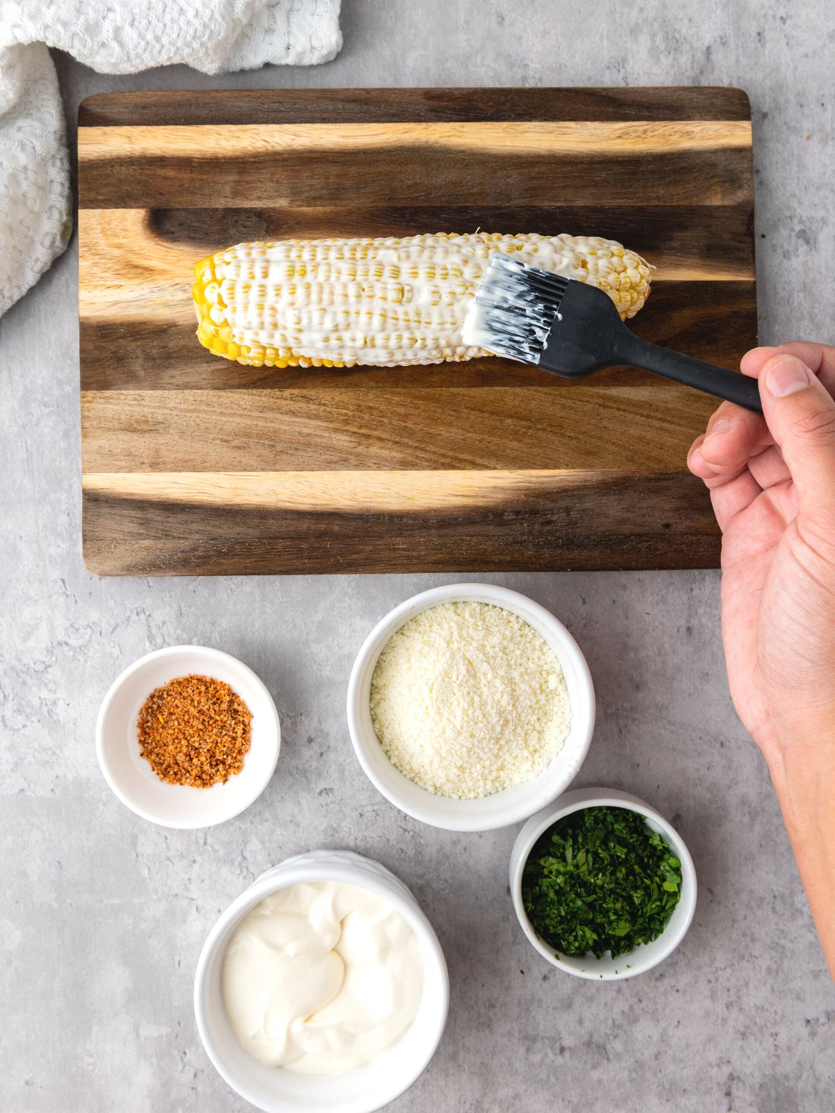 Spreading mayonnaise mixture over an ear of corn with a pastry brush to make elote. 