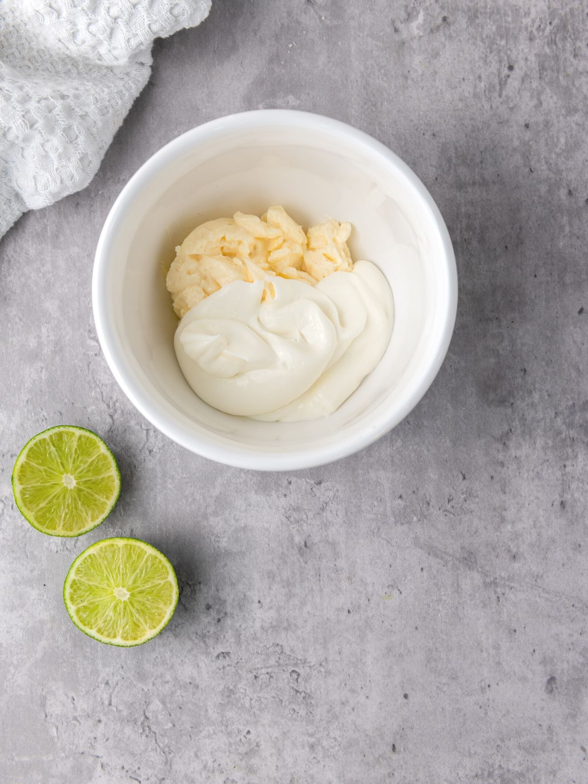 Bowl filled with crema and mayonnaise with two lime halves ready to be squeezed in.