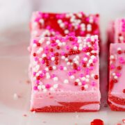 Four squares of pink and red swirl strawberry fudge with sprinkles.