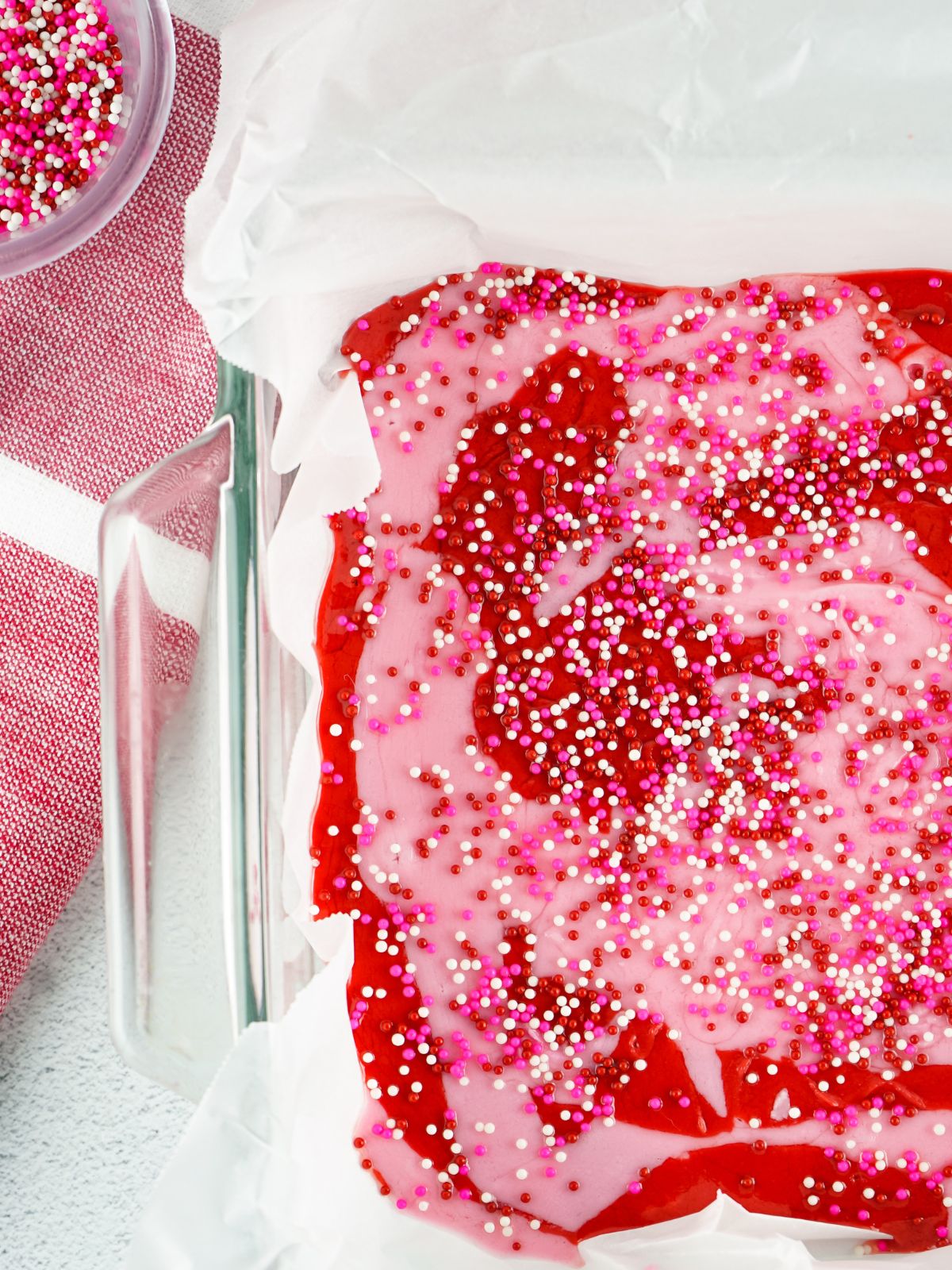 Pink and red fudge swirled together in a pan with sprinkles on top.
