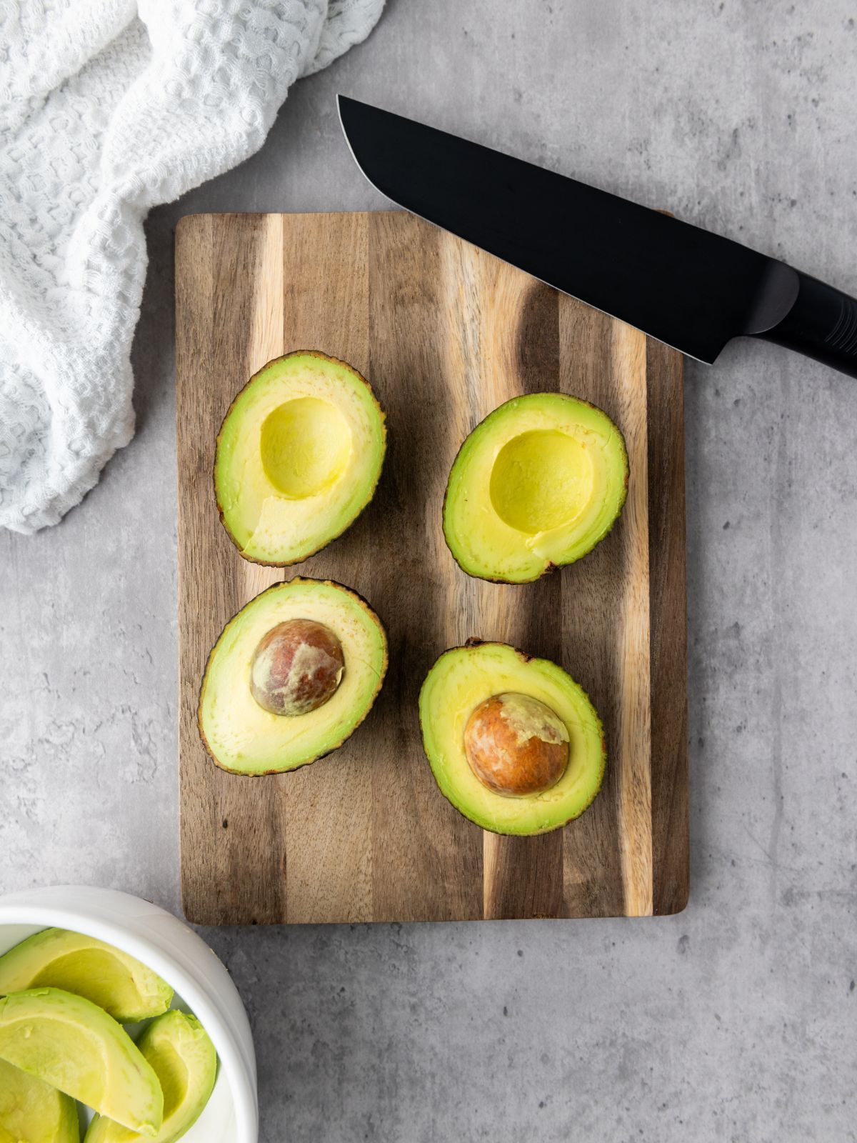 Two avocados sliced into four halves on a wooden cutting board.