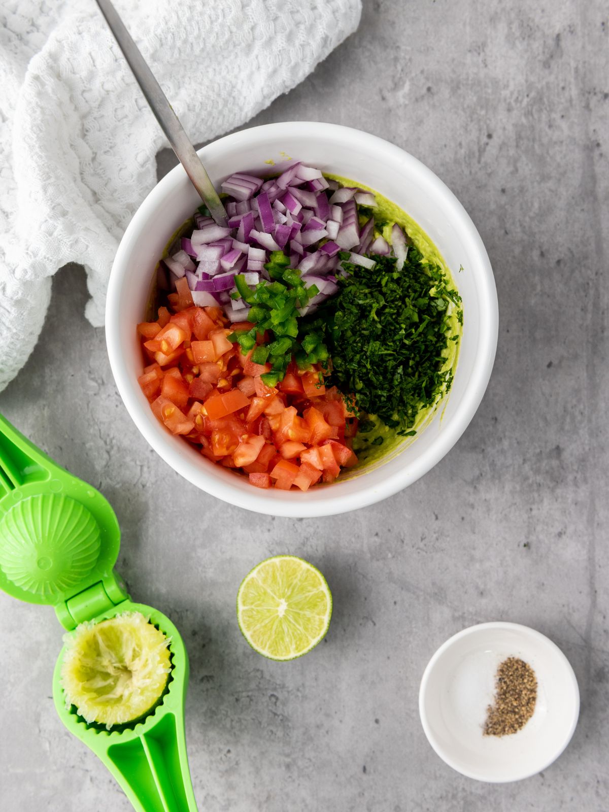 Adding the diced tomatoes, diced onion, chopped jalapeno, chopped cilantro, juice of the lime and season with salt and pepper to the mashed avocado.