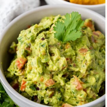 A bowl of prepared guacamole garnished with cilantro with chips in the background.